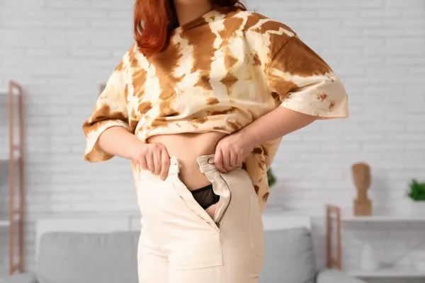 Image of woman trying to do her trousers up after pregnancy weight gain Robroyston