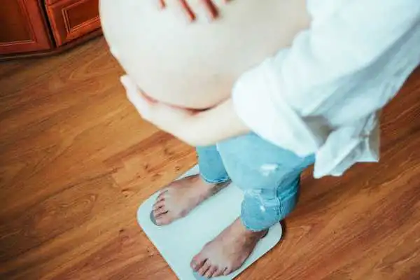Image of woman weighing herself and experiencing weight gain through pregnancy Robroyston